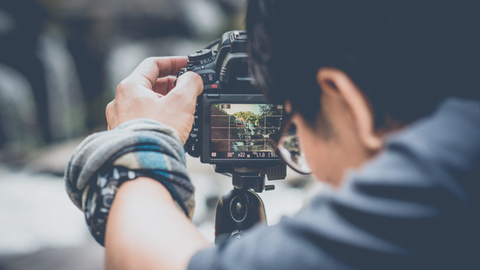 Videographer capturing a scene on a tripod | Aris Suwanmalee | Shutterstock.com